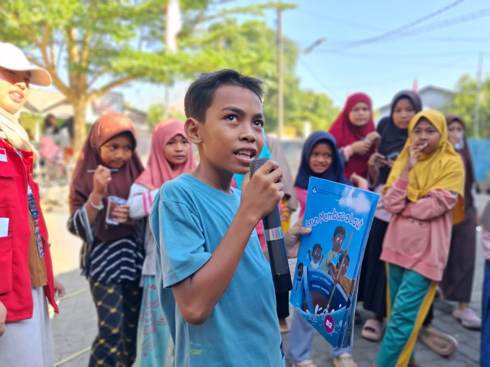 
Seorang anak dengan percaya diri memegang mikrofon dan sebuah buku, saat ia berpartisipasi dalam lomba mengulas buku. Lomba ini merupakan bagian dari kegiatan Apresiasi Literasi yang diadakan oleh mahasiswa KKN Unhas Gelombang 114 di Desa Tamasaju, Takalar. Kegiatan ini bertujuan untuk meningkatkan kemampuan literasi dan minat baca anak-anak desa. Kredit: Mahasiswa KKN Unhas.